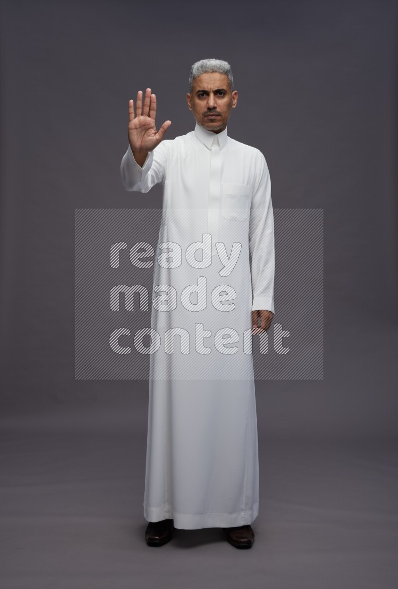 Saudi man wearing thob standing interacting with the camera on gray background