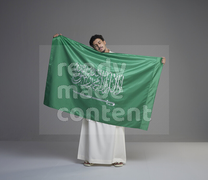 رجل سعودي يرتدي ثوب ابيض ويحمل العلم السعودي