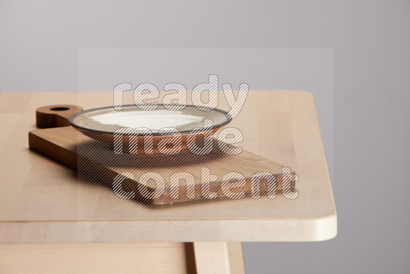 multi-colored pottery Plate placed on a  wooden rectangular cutting board on the edge of wooden table
