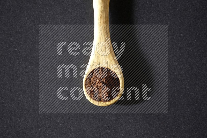 A wooden spoon full of cloves powder on a black flooring