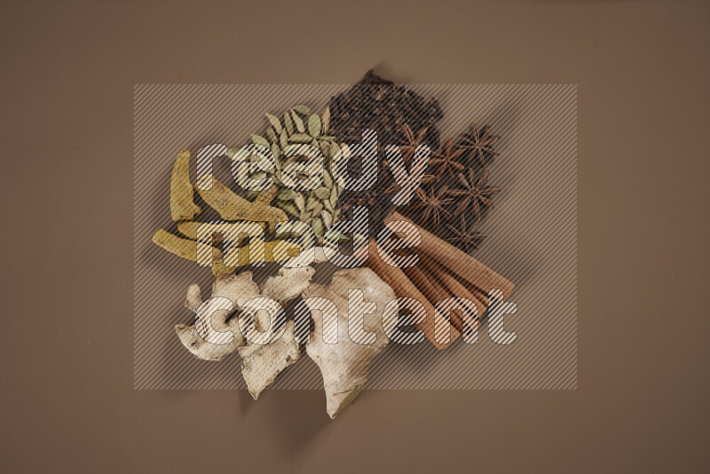 An assorted whole spices including fresh and dried ginger, cinnamon sticks, cardamom, turmeric fingers, cloves, star anise on beige background