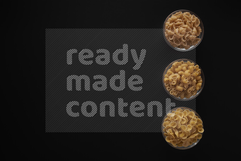 Different pasta types in 3 glass bowls on black background