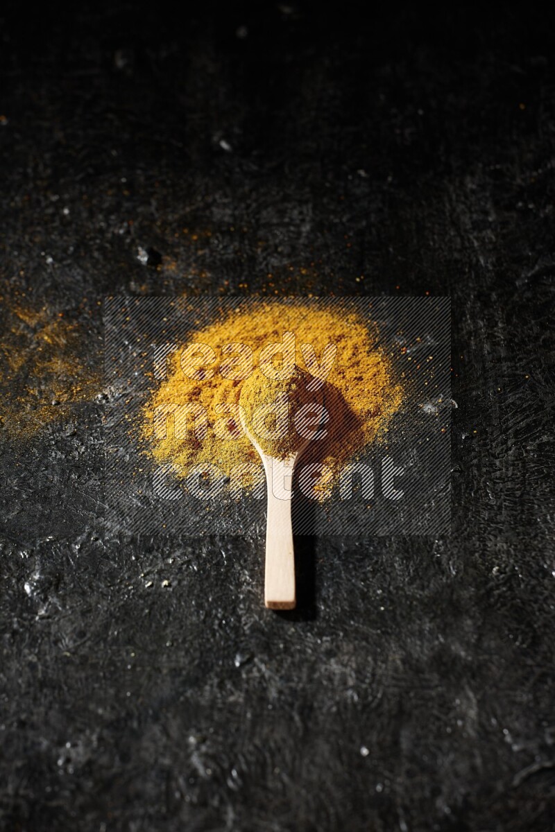 A wooden spoon full of turmeric powder on textured black background
