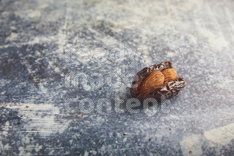 one almond stuffed madjoul dates on a rustic blue background