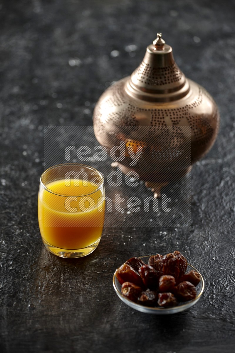 A golden lantern with different drinks, dates, nuts, prayer beads and quran on textured black background