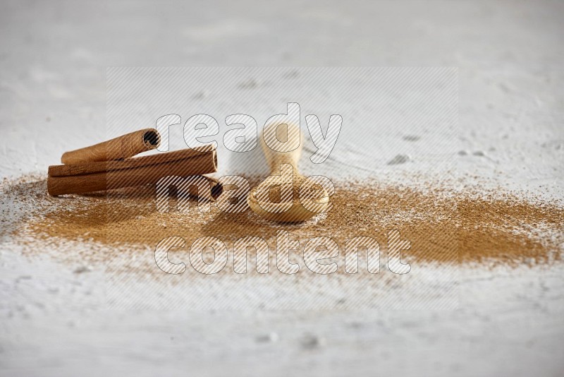 Cinnamon powder in a wooden spoon with cinnamon sticks and sprinkles powder on the flooring on white background