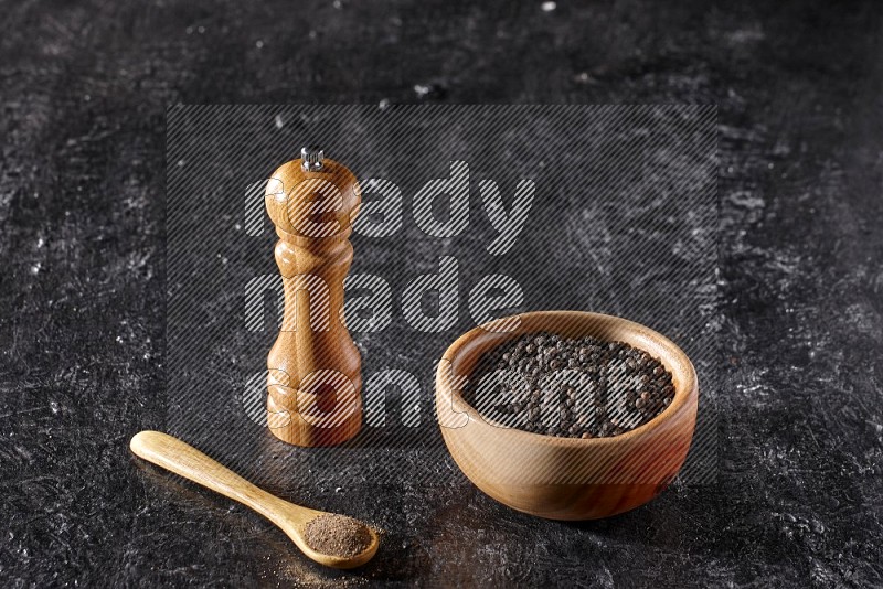 الفلفل الأسود في وعاء وملعقة خشبية مع مطحنة خشبية علي خلفية سوداء