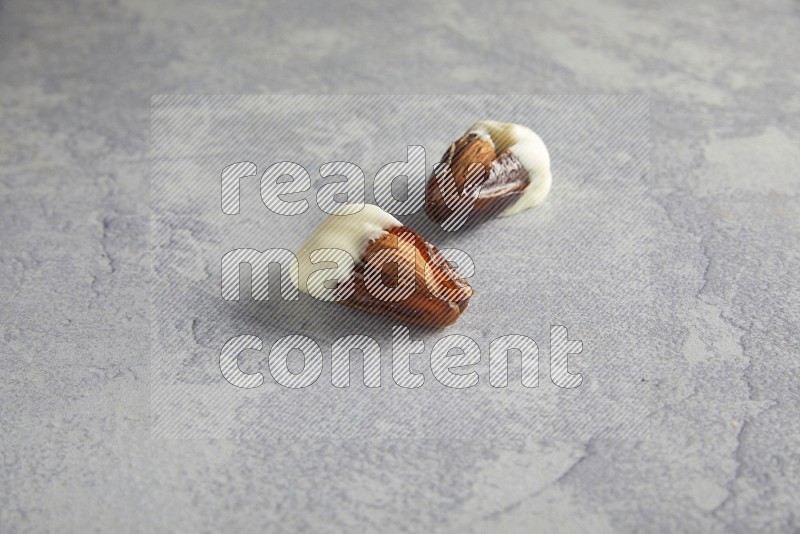 two almonds stuffed dates covered with white chololate on a light grey background