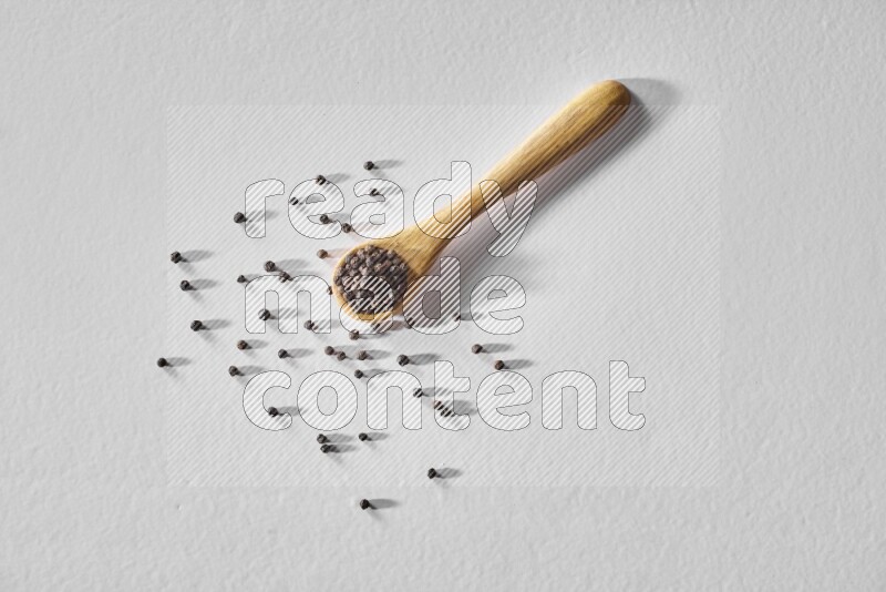 حبوب الفلفل الأسود في ملعقة خشبية علي خلفية بيضاء