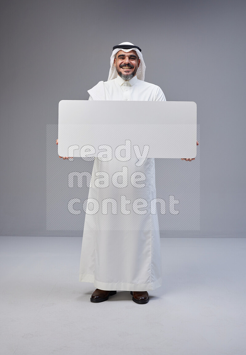 Saudi man Wearing Thob and white Shomag standing holding board on Gray background
