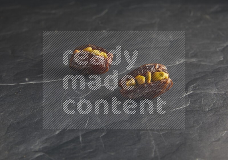 two pistachios stuffed madjoul dates on a black textured background