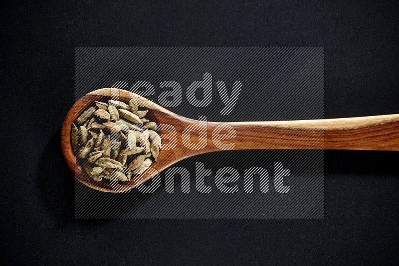A wooden ladle full of cardamom on black flooring