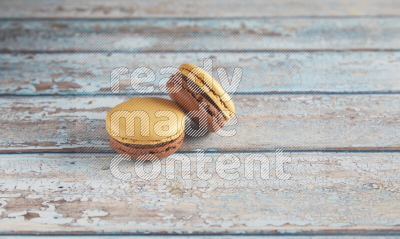 45º Shot of two Yellow and Brown Chai Latte macarons on light blue wooden background