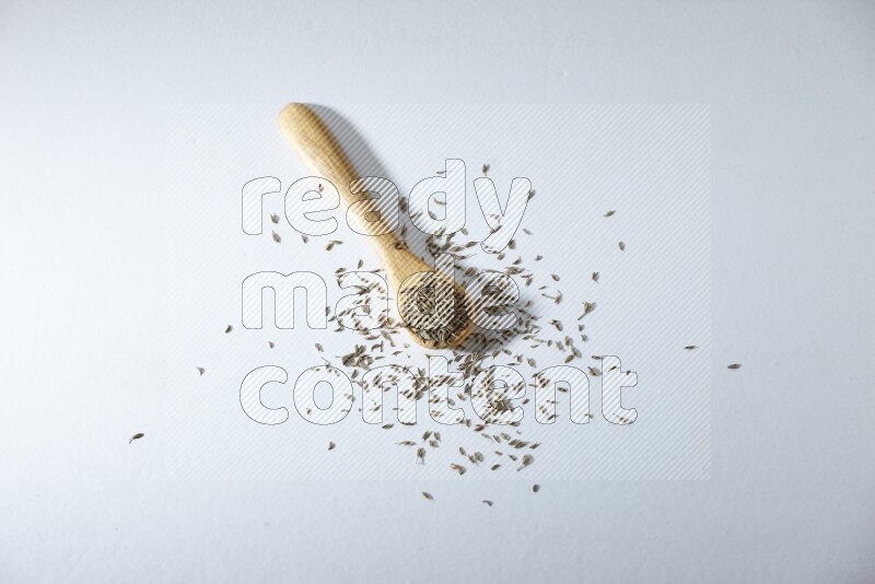 A wooden spoon full of cumin seeds on a white flooring