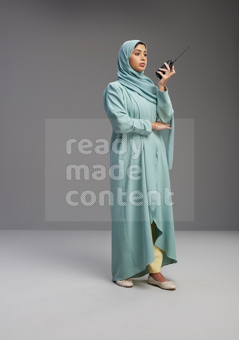 Saudi Woman wearing Abaya standing holding walkie-talkie on Gray background