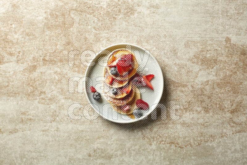 Five stacked mixed berries mini pancakes in a blue plate on beige background