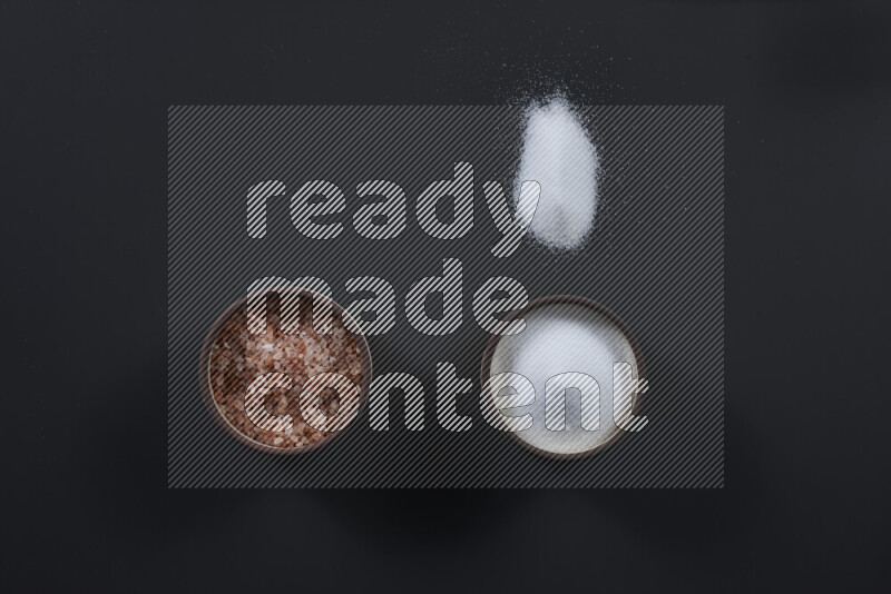 2 وعاء فخاري احدهمها ممتلئ بملح الهيمالايا والأخر بالملح الأبيض على خلفية سوداء