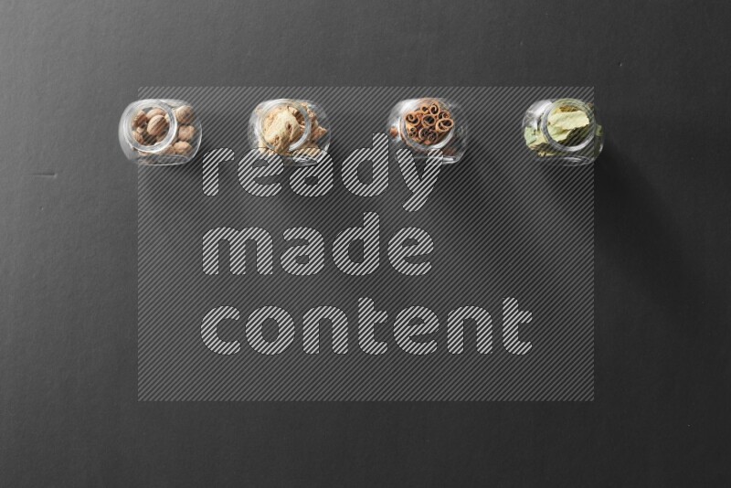 أوراق الغار وزنجبيل مجفف وقرفة وجوزة الطيب في أوعية زجاجية علي خلفية سوداء