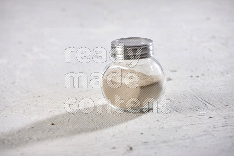 A glass spice jar full of garlic powder on a textured white flooring