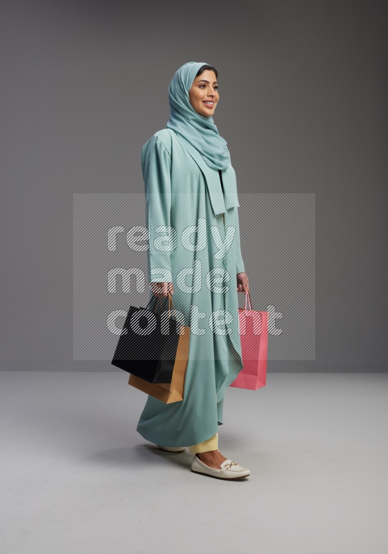Saudi Woman wearing Abaya standing holding shopping bag on Gray background