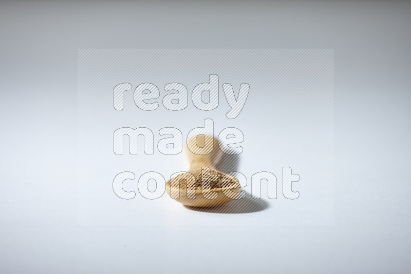 A wooden spoon full of cumin powder on a white flooring