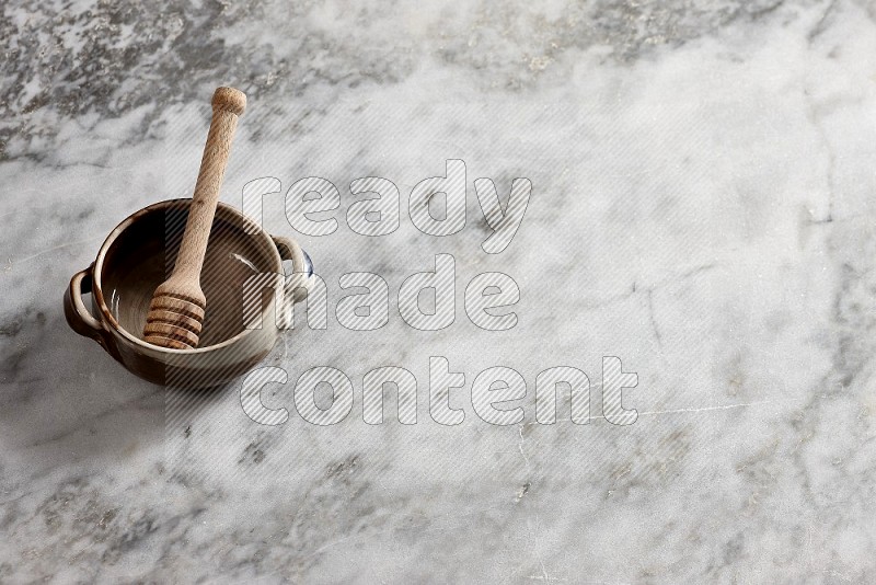 Multicolored Pottery bowl with wooden honey handle in it, on grey marble flooring, 65 degree angle