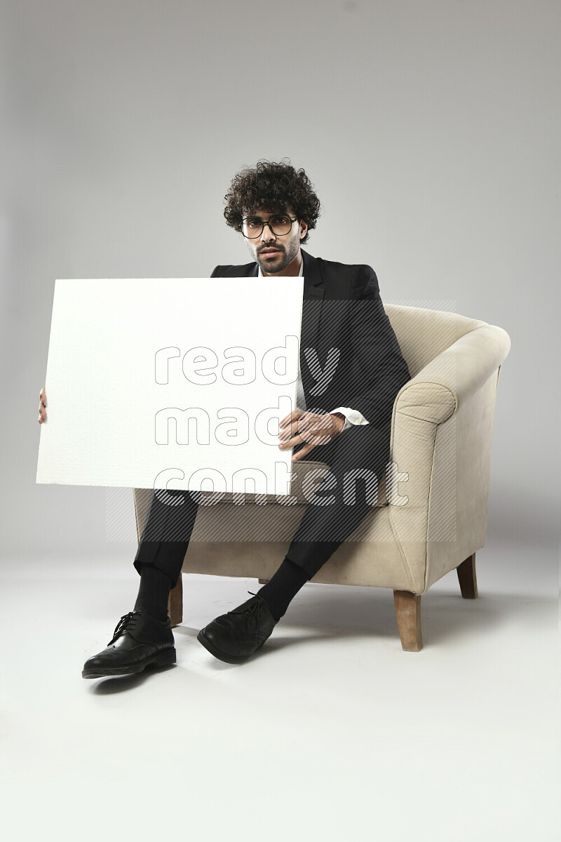 A man wearing formal sitting on a chair holding a white board on white background