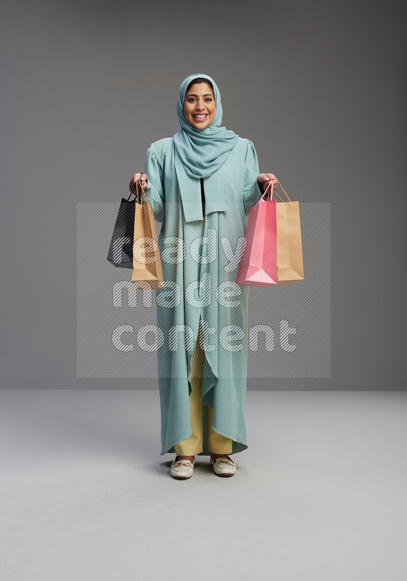 Saudi Woman wearing Abaya standing holding shopping bag on Gray background