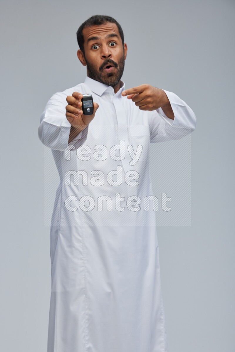 Saudi man wearing thob and shomag standing holding car key on gray background