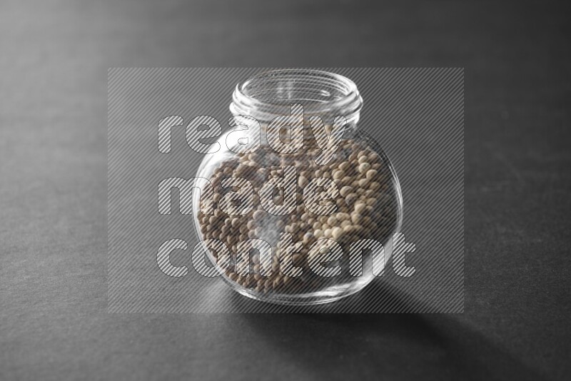 A glass spice jar full of white peppers on black flooring