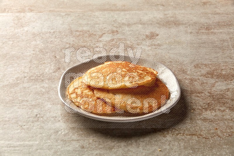 Three stacked plain pancakes in an irregular plate on beige background
