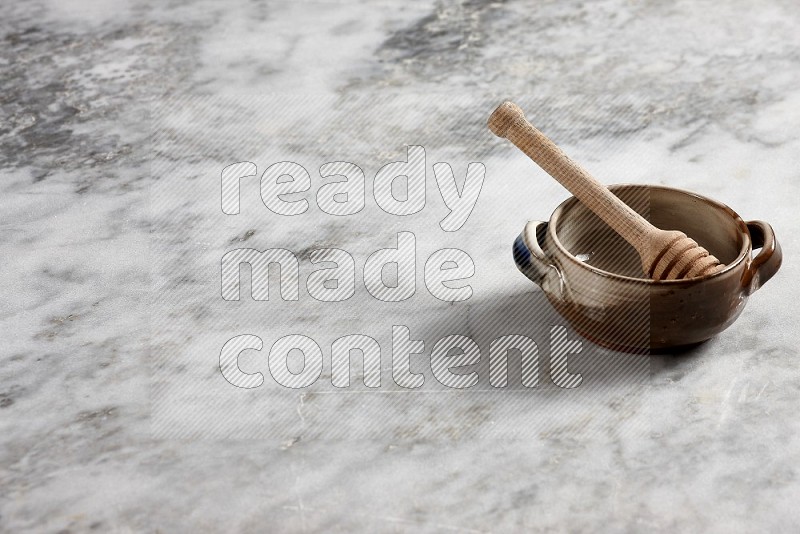 Multicolored Pottery bowl with wooden honey handle in it, on grey marble flooring, 45 degree angle