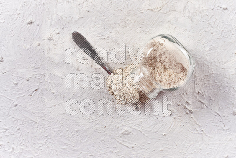 A glass jar full of onion powder flipped with some spilling powder on white background