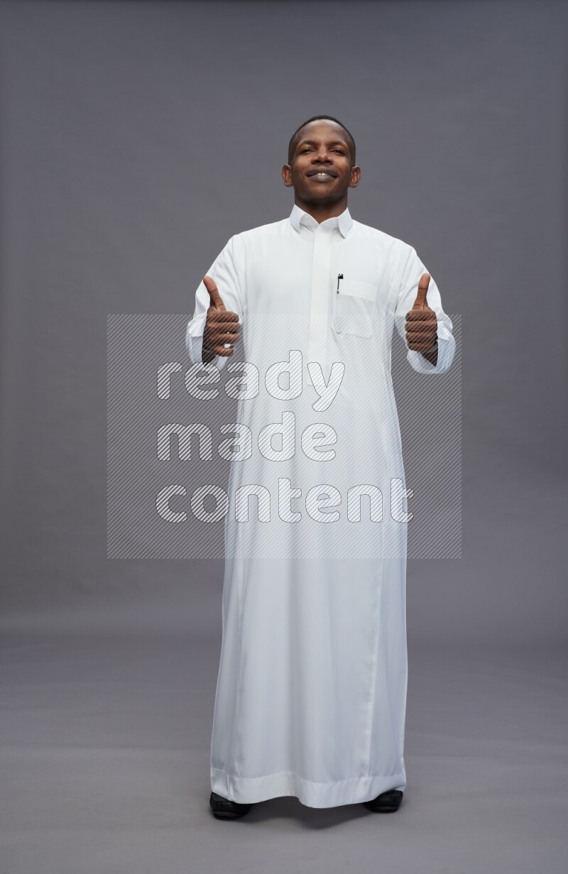 Saudi man wearing thob standing interacting with the camera on gray background