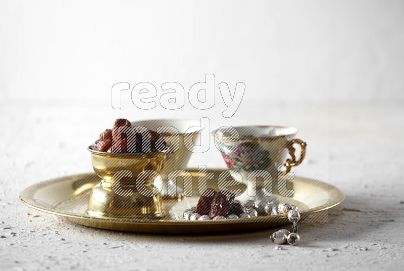 تمر في وعاء معدني مع شاي وسبحة على صينية معدنية علي خلفية بيضاء