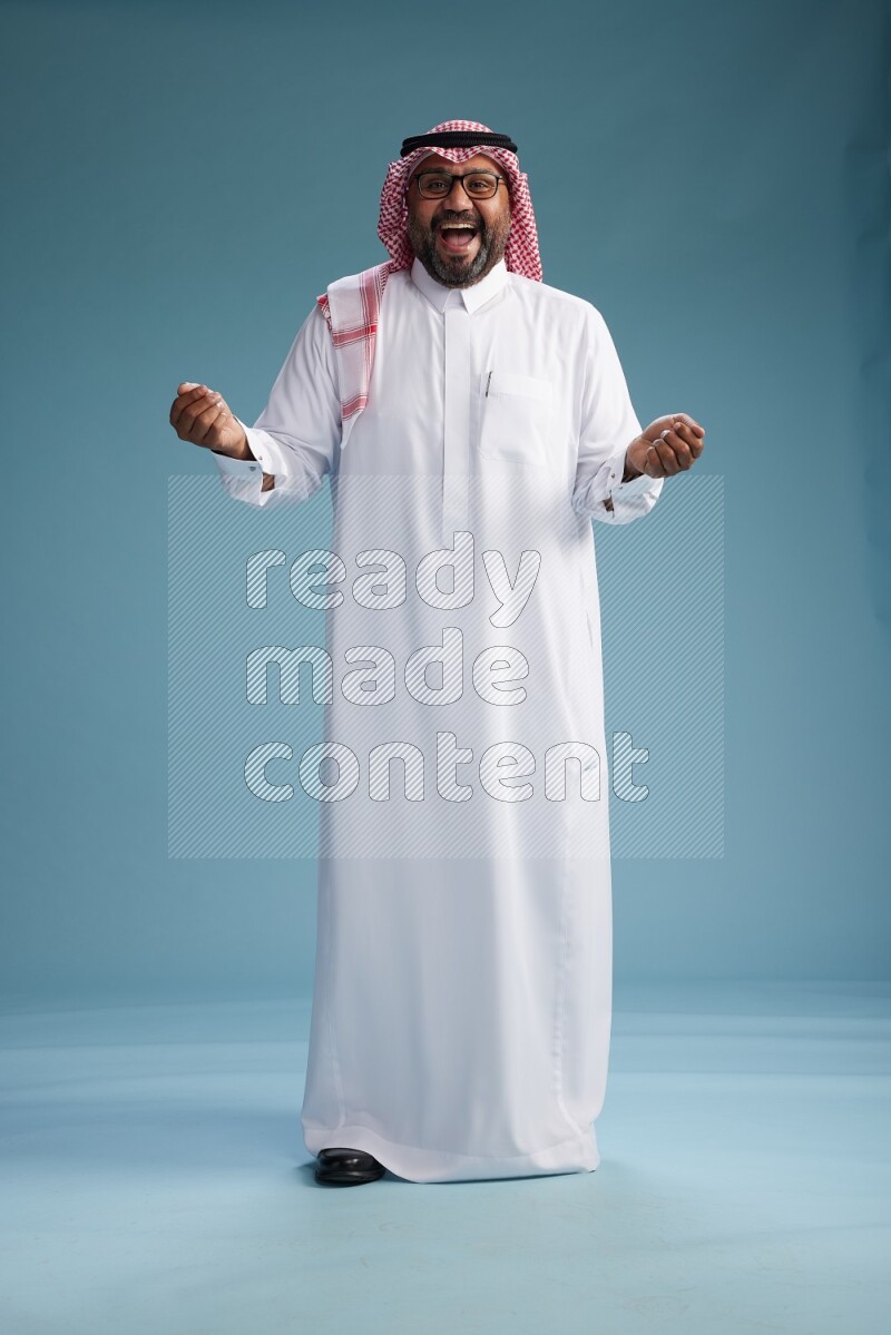 Saudi Man with shimag Standing Interacting with the camera on blue background