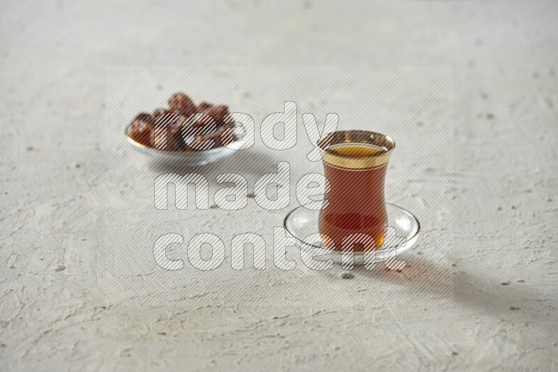 A tea glass cup with dates and coffee on textured white background