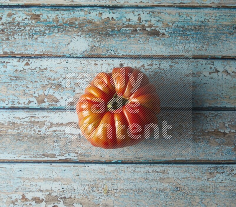 Single topview Heirloom tomato on a blue rustic wooden background