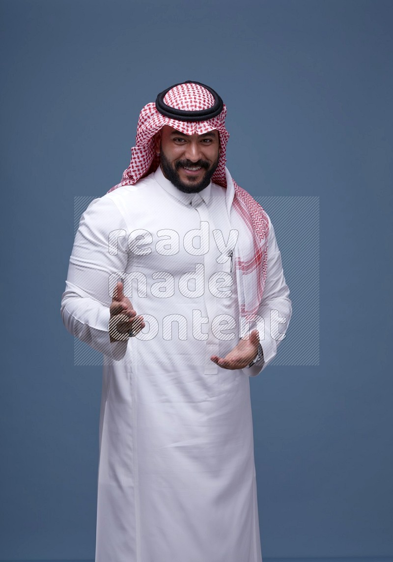 A man pointing on blue background wearing Saudi Thob with Shomag