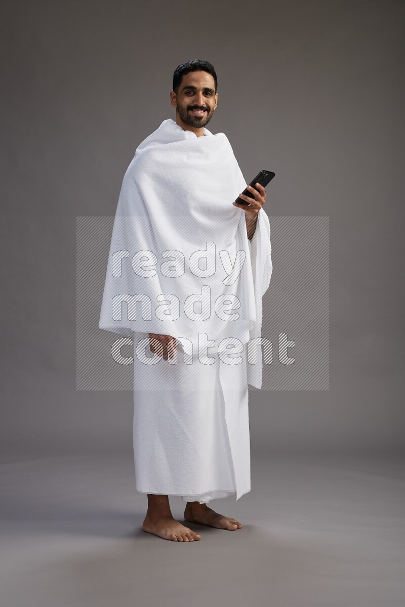 A man wearing Ehram Standing texting on phone on gray background