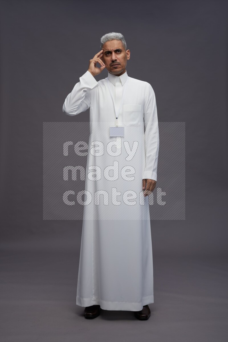 Saudi man wearing thob with neck strap employee badge standing interacting with the camera on gray background