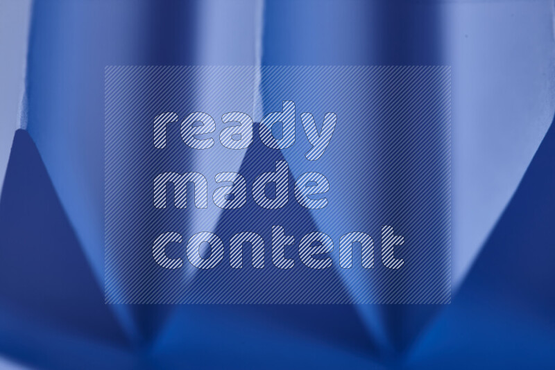 صورة مجردة مقربة تظهر طيات ورقية هندسية حادة بتدرجات اللون الأزرق