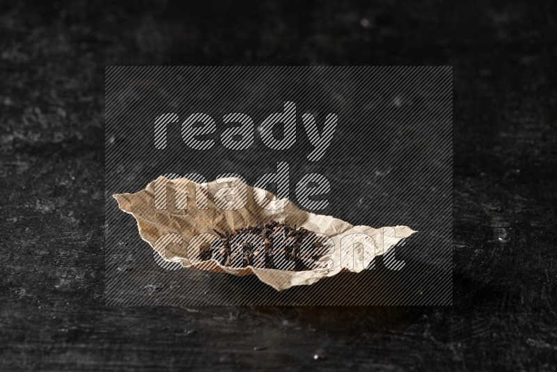 Cloves in crumpled piece of paper on a textured black flooring