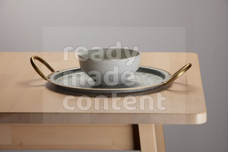grey bowl placed on a rounded stainless steel tray with golden handels on the edge of wooden table