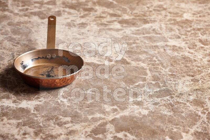 A small copper pan on beige marble background
