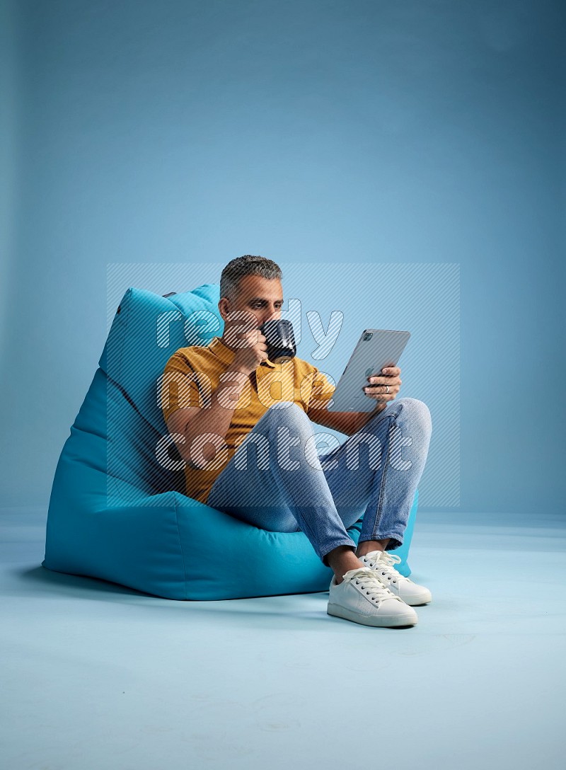 A man sitting on a blue beanbag and drinking coffee