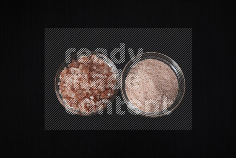 2 glass bowls one is filled with fine himalayan salt and the other with coarse himalayan salt on black background