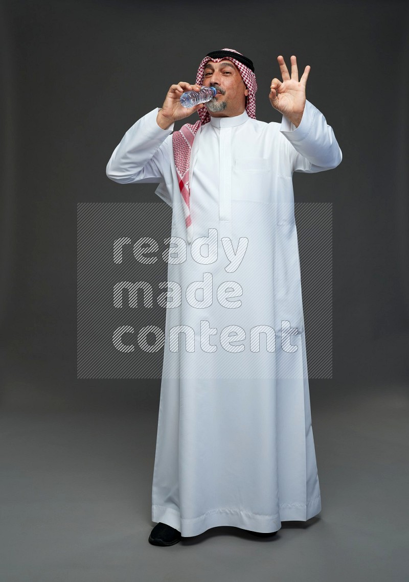 Saudi man with shomag Standing drinking water on gray background