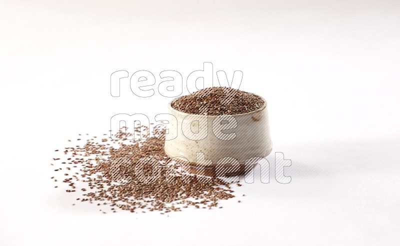 وعاء بيج فخاري ممتلئ بحبوب بذر الكتان مع بعض الحبوب المتناثرة علي خلفية بيضاء