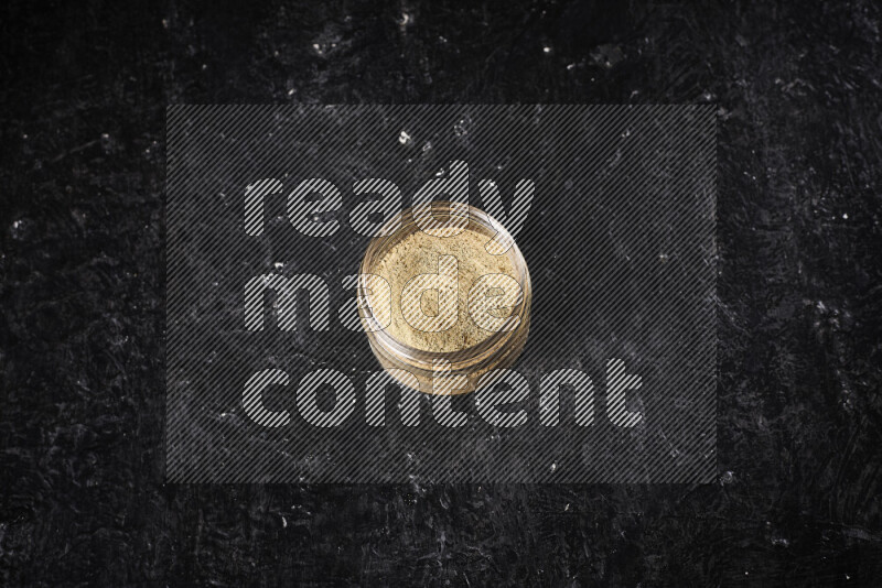 A glass jar full of ground ginger powder on black background